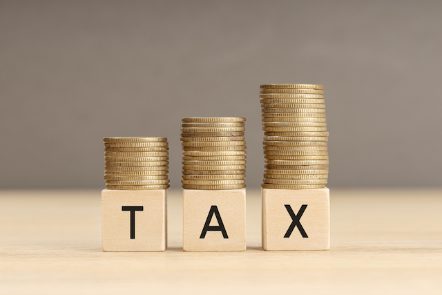 Tax word in wooden blocks with coins stacked in increasing stacks. Tax increasing concept. Copy space